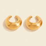 Two polished gold-tone ear cuffs sit on a warm cream background, with C-shaped openings and soft shadows.