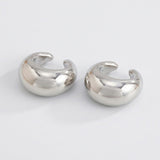 Two polished silver-tone ear cuffs rest on a light gray background, with rounded profiles and open C-shaped designs.