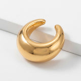 A polished gold-tone ear cuff rests beside a raised white edge, with its C-shaped opening facing upward.