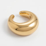 A gold-tone ear cuff rests at an angle on a white background, showing its wide curved face and rounded ends.