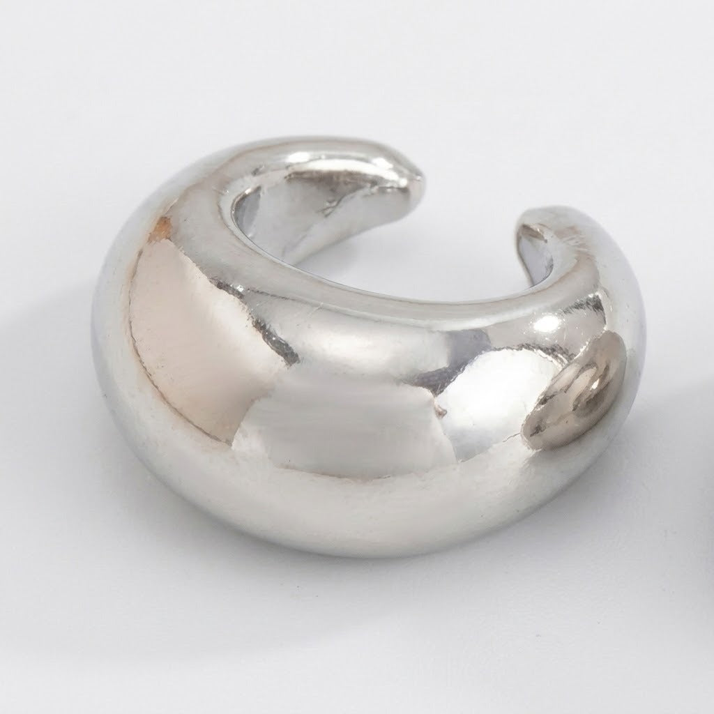 A polished silver-tone ear cuff rests on a white background, showing its broad reflective face and C-shaped opening.