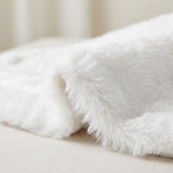 A close-up shows the white tree skirt folded on a cream surface, highlighting its fluffy pile and fabric backing.