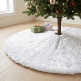 A white fluffy tree skirt surrounds a decorated Christmas tree on a pale wooden floor, with two wrapped gifts near the trunk.