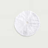 White plush Christmas tree skirt laid flat on a pale background, showing a round shape, center hole, and opening slit.