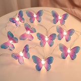 Glowing pink and blue butterfly string lights lie loosely across a round cream tabletop beside peach curtains.
