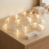 Clear butterfly string lights glow warm yellow on a wooden dresser beside a transparent battery box, mirror, and cream storage box.
