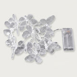 Unlit clear butterfly string lights with patterned wings and silver wire lie beside a transparent battery box on a white background.
