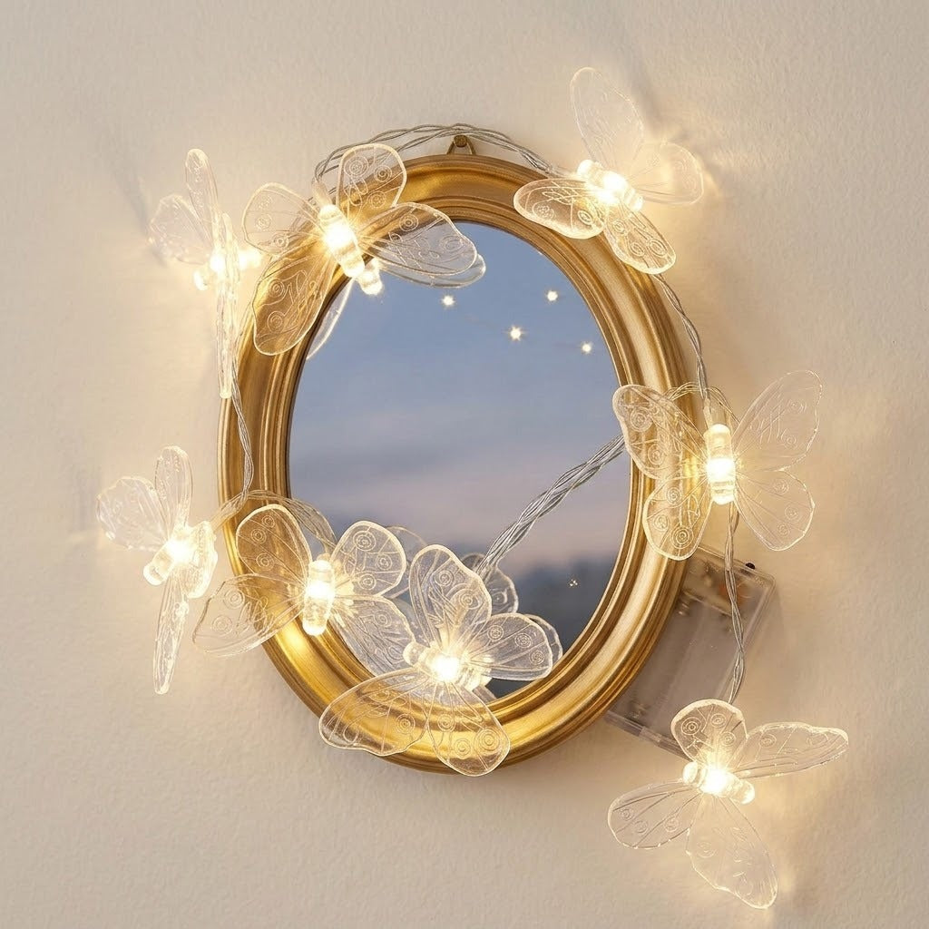 Clear butterfly string lights wrap around an oval gold-framed mirror on a cream wall, with a transparent battery box alongside.