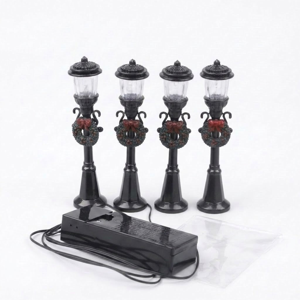 Four unlit black miniature street lights with clear lanterns, wreaths, and red bows connect to a battery box against a white background.