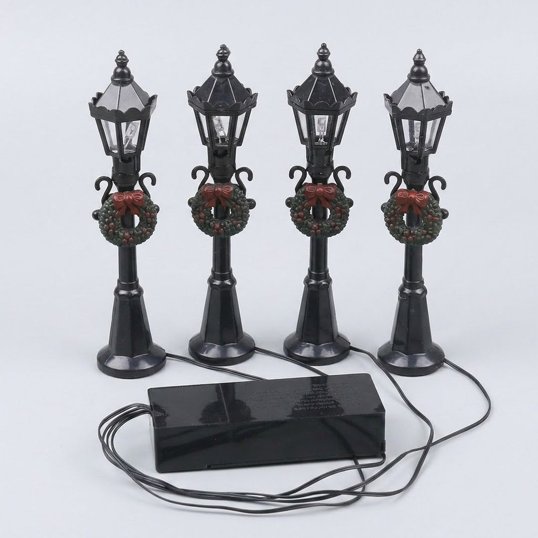 Four black plastic miniature street lights with pointed lanterns, green wreaths, and red bows connect to a battery box on a pale background.