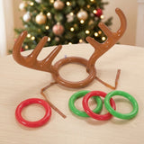 Reindeer ring toss game with brown inflatable antlers and four red and green rings on a light wooden table before a Christmas tree.