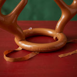 Close-up of the ring toss game's brown inflatable antler headgear and loose straps on a red surface against a dark green background.