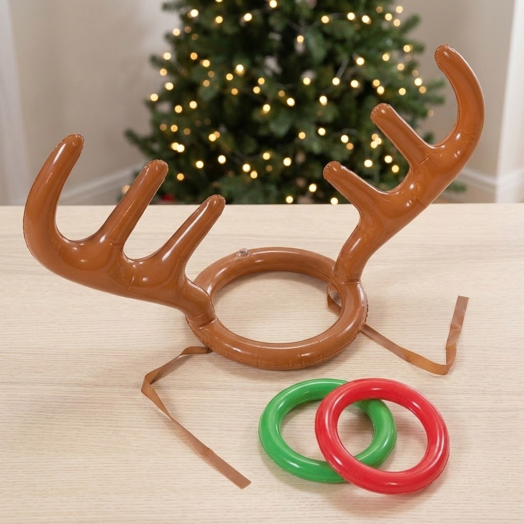 Ring toss game with brown inflatable antler headgear and two red and green rings on a pale wood table before a lit Christmas tree.