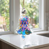 An iridescent bell-shaped glass suncatcher with vivid blue and pink reflections hangs above a white countertop beside sunlit kitchen windows.