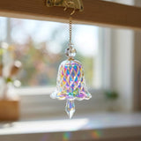 A rainbow iridescent glass suncatcher hangs from a gold-tone hook and chain on a wooden window frame against a blurred interior.