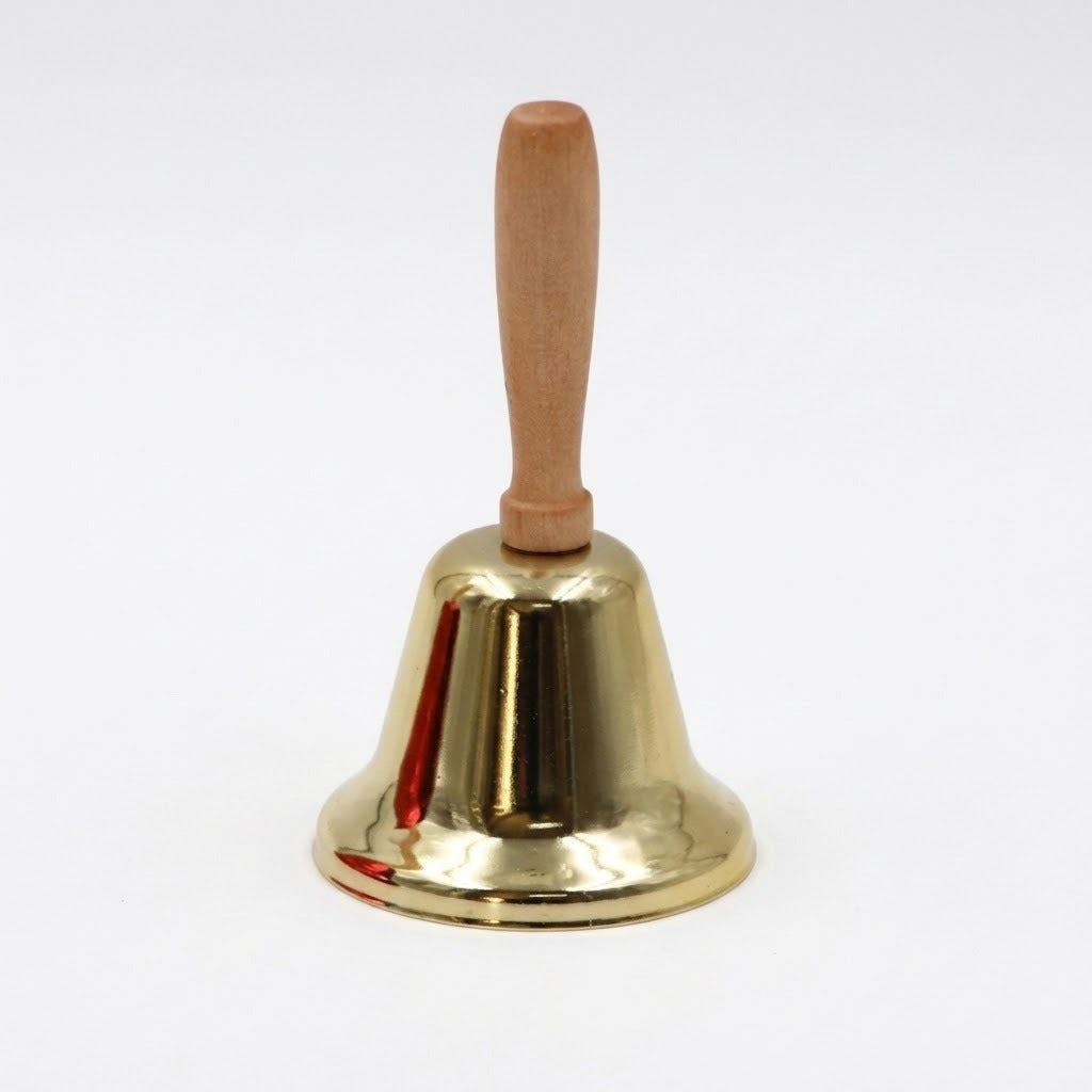 A gold hand bell with a light wooden handle and flared rim stands upright against a plain white background.