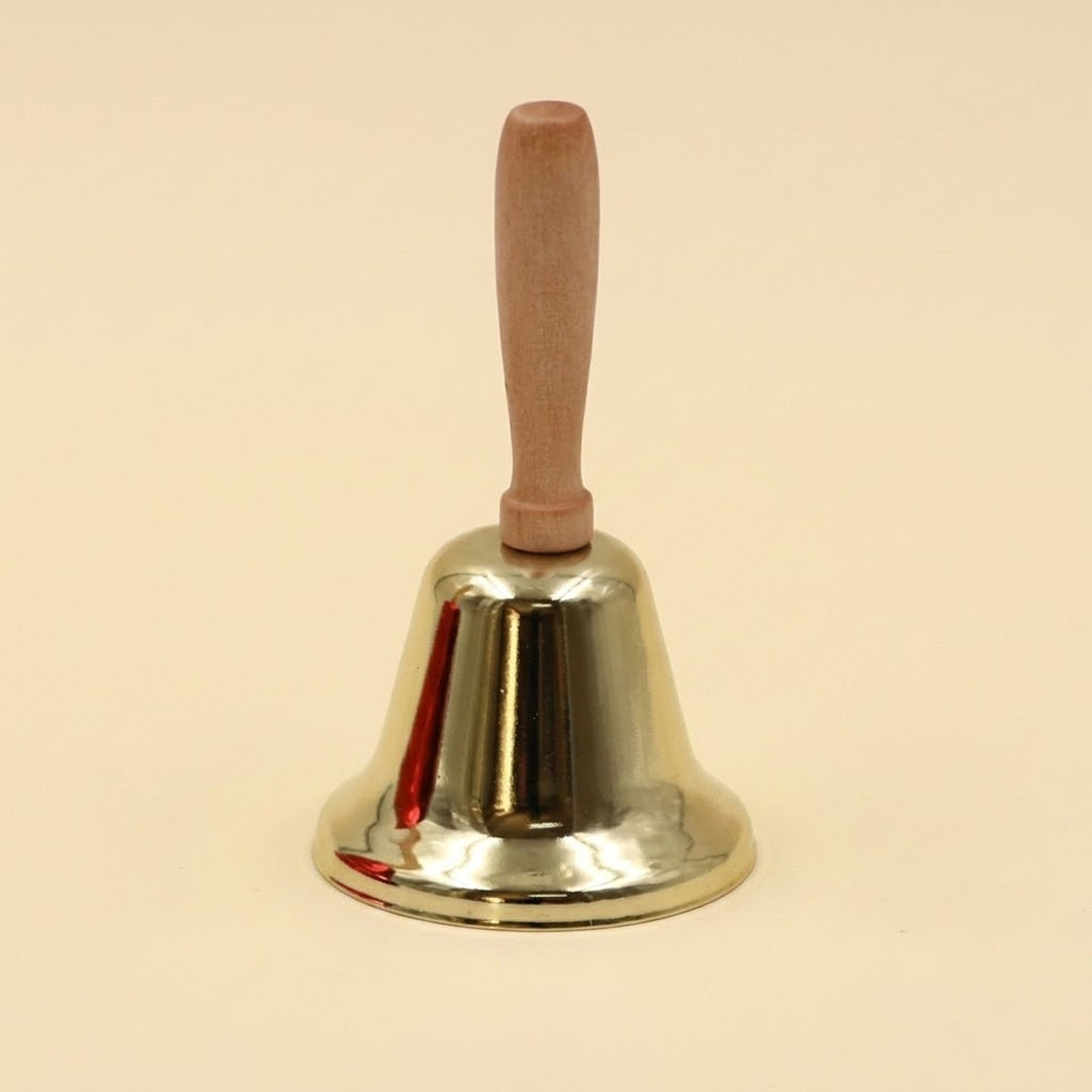 A shiny gold iron hand bell with a light wooden handle stands upright against a pale cream background.