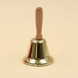 A shiny gold iron hand bell with a light wooden handle stands upright against a pale cream background.
