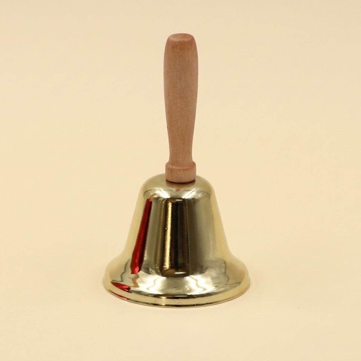 A shiny gold iron hand bell with a light wooden handle stands upright against a pale cream background.