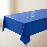 A blue tablecloth drapes over a rectangular table beside a bright window, with water droplets and an upright clear glass.
