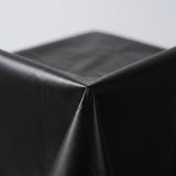 A glossy black tablecloth folds over a table corner against a pale background.