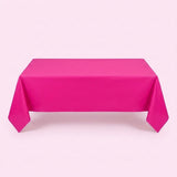 A hot pink tablecloth covers a rectangular table with long pointed corner folds against a pale pink background.