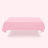 A light pink tablecloth drapes over a rectangular table with hanging corners against a pale pink background.