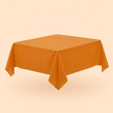 An orange tablecloth covers a table viewed diagonally, with pointed hanging corners against a pale peach background.