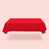 A plain red tablecloth covers a rectangular table with draped sides and folded corners against a pale pink background.