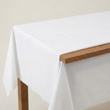 A white tablecloth with water droplets drapes over a wooden table, leaving part of the brown edge exposed.