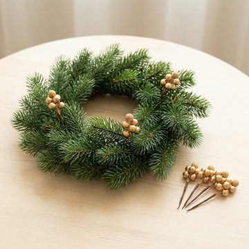 Gold berry picks decorate a green wreath on a pale wooden table, with loose picks arranged beside it.