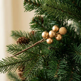 A gold berry pick with smooth and glittered berries rests among green evergreen branches and brown pinecones.