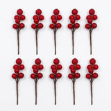 Ten red berry picks with brown stems and glittered top berries form two rows on a white background.