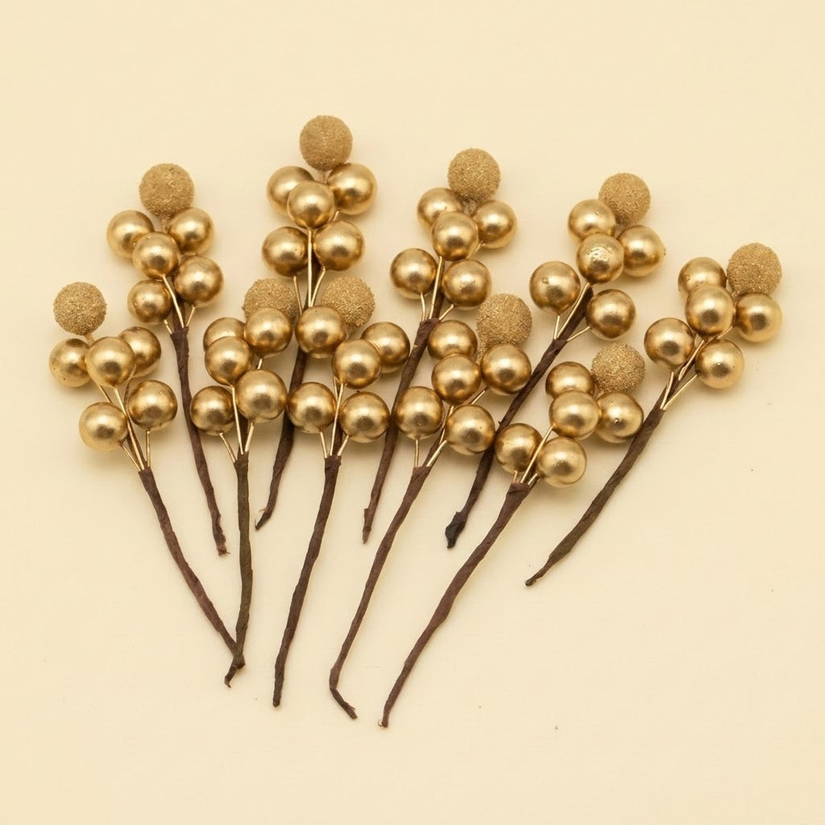 Gold foam berry picks with smooth and glittered berries on brown stems fan across a cream background.
