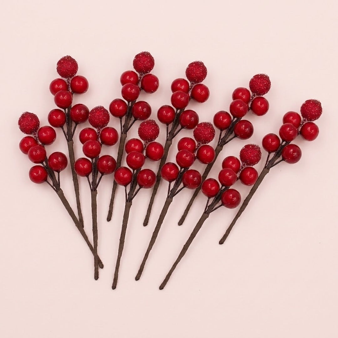 Red foam berry picks with glossy and glittered berries on brown stems fan across a pale pink background.