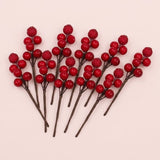 Red foam berry picks with glossy and glittered berries on brown stems fan across a pale pink background.