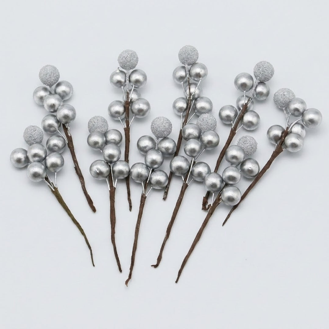 Silver foam berry picks with smooth and glittered berries on brown stems fan across a light grey background.