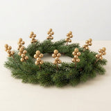 Gold berry picks stand upright around a green evergreen wreath lying on a cream surface against a plain background.