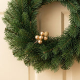 A gold berry pick with smooth and glittered foam berries decorates a green evergreen wreath on a cream paneled door.