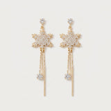 Gold-tone drop earrings with rhinestone snowflakes, dangling chains, clear stones, and slender bar tassels lie on a white background.