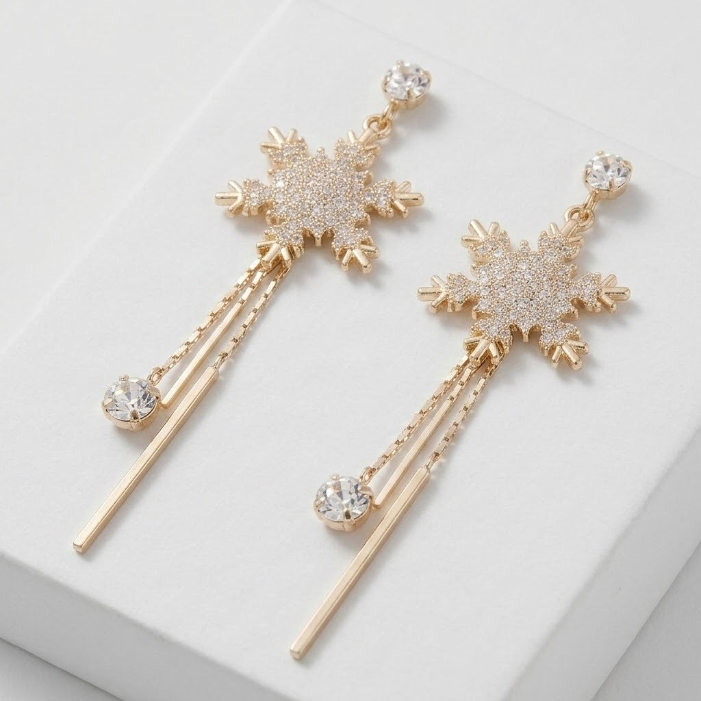 A pair of gold-toned snowflake dangle earrings with clear crystal rhinestone detailing and long drop chains ending in round clear crystal beads, displayed on a clean white surface.