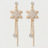Gold-toned snowflake drop earrings with clear rhinestones and long chain tassels lie side by side against a plain white background.