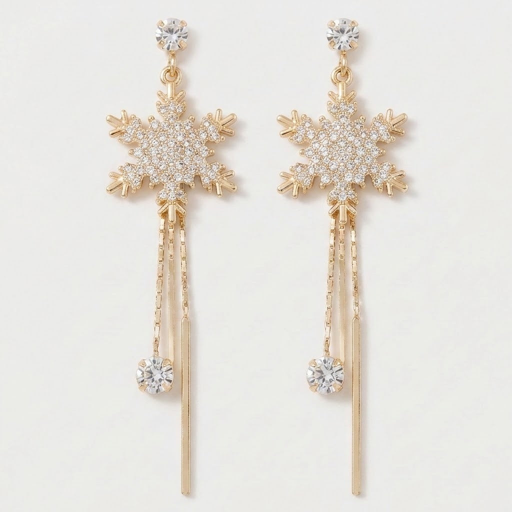 Gold-toned snowflake drop earrings with clear rhinestones and long chain tassels lie side by side against a plain white background.