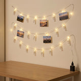 Warm white photo clip lighting with clear clips displays scattered photographs on a beige wall above a wooden table.