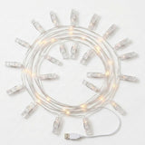 Photo clip lighting with clear plastic clips and warm white lights lies coiled on a white background beside its USB plug.