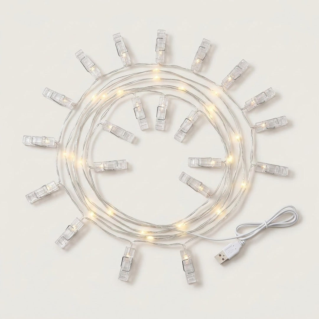 Warm white photo clip lighting with clear clips and silver-colored wire lies coiled beside a white USB cable on a white background.