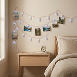 Cool white photo clip lighting displays landscape photographs on a bedroom wall above a wooden nightstand beside a bed.