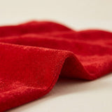 Close-up of a red velvet gift sack shows its plush texture, stitched edge, and soft folds against a cream background.