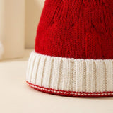 Close-up of a red knit santa hat with a white ribbed cuff and red edging against a cream background.