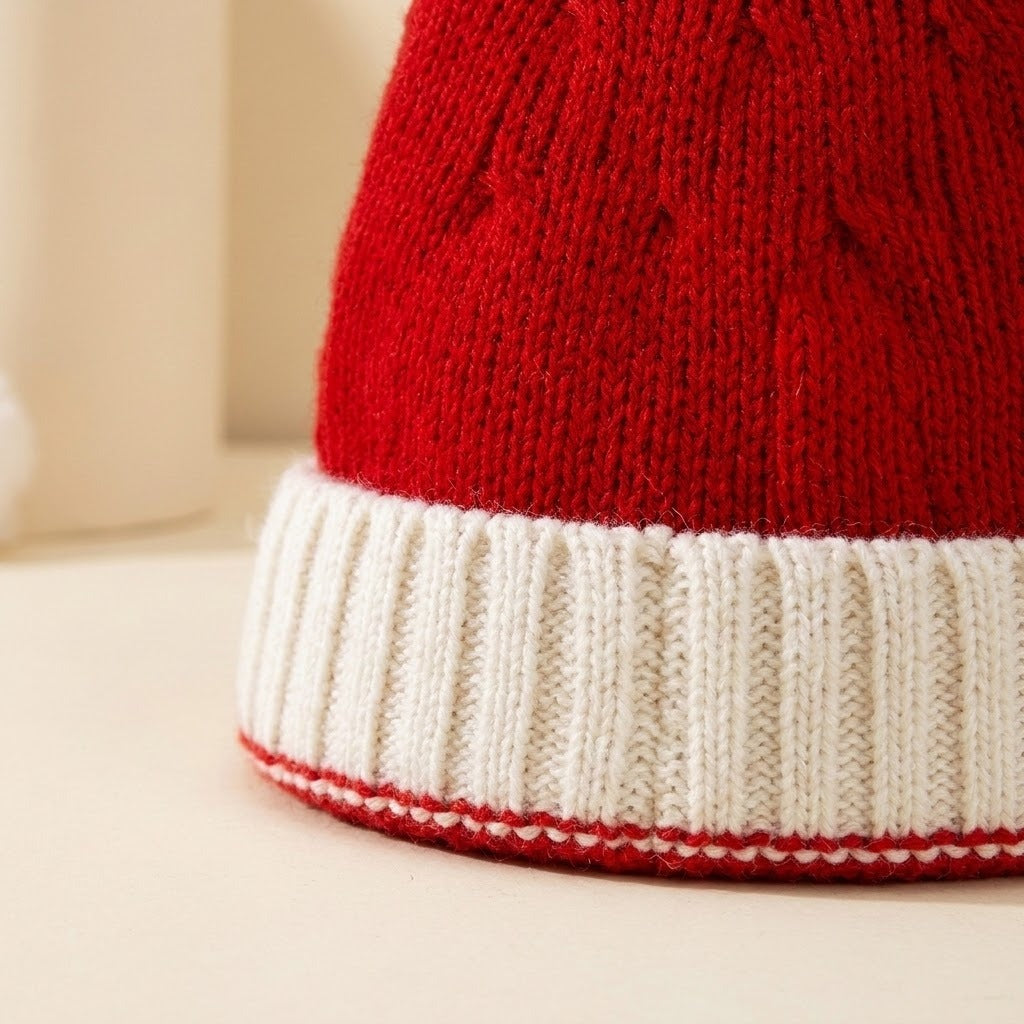 Close-up of a red knit santa hat with a white ribbed cuff and red edging against a cream background.